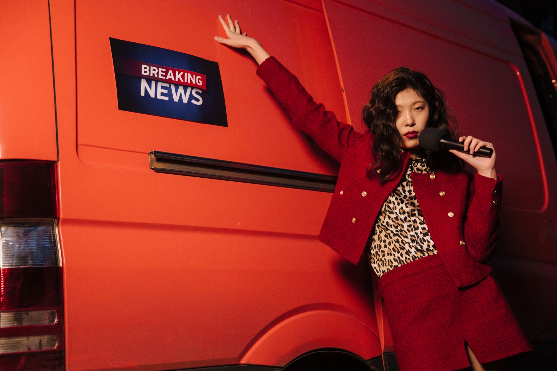 Fashionable reporter with microphone posing dramatically next to a news van. — test123123