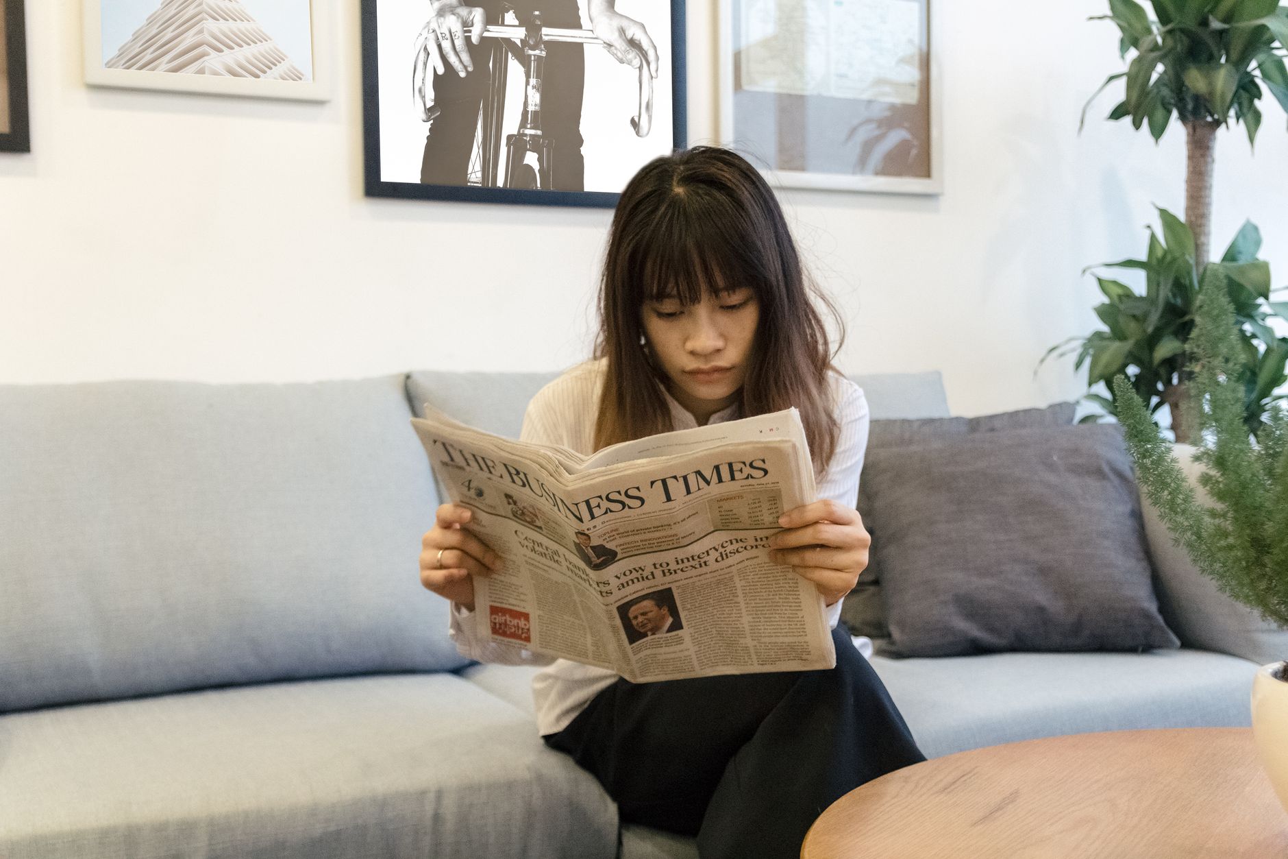 A young woman attentively reads a newspaper while sitting on a modern sofa indoors. — Welchen Einfluss hat die Technologie au